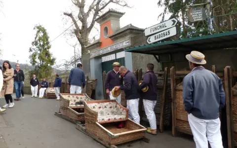 Korbschlitten Madeira: Männer in traditioneller Kleidung warten neben den Korbschlitten auf Fahrgäste.