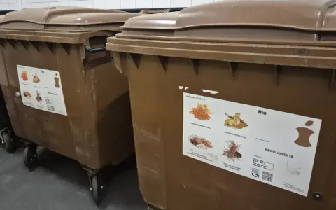 Brązowe kontenery na odpady bio. Naklejka informuje, co można wyrzucać, sugerując, że odpady bio można wyrzucać w workach.