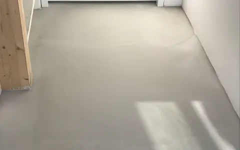 Pavimento in resina grigia, simile a un massetto, con un pilastro di legno. Potrebbe essere un'idea per pavimenti in pvc svantaggi, ma questa è una finitura grezza.