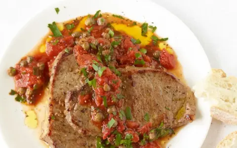 Zwei saftige Scheiben Rindfleisch, bedeckt mit einer würzigen Tomaten-Kapern-Sauce, serviert mit Brot. Ein authentisches Gericht im Stil Pizzaiola original italienisch.