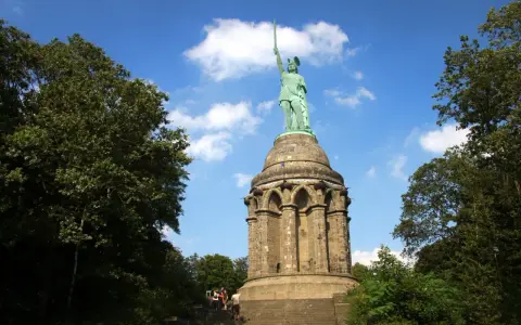 Aufstieg zum Hermannsdenkmal: Wanderer erklimmen die Stufen zum imposanten Reiterstandbild unter blauem Himmel.