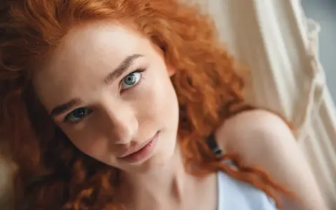 Primer plano de una joven con cabello castaño pelirrojo natural y ojos azules, recostada en una hamaca.