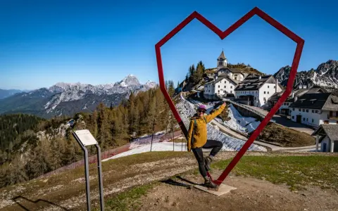 Kobieta w sercu z widokiem na górską wioskę Monte Lussari.