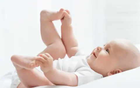 Uśmiechnięte dziecko leży na plecach, podnosząc nóżki. Czas na zmianę pampersów na większe, gdy maluch rośnie.
