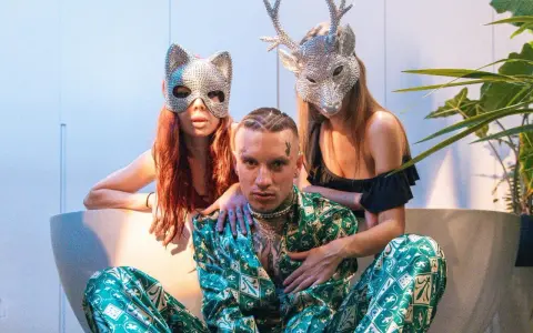 Smolasty z dużymi oczami w otoczeniu dwóch kobiet w błyszczących maskach.