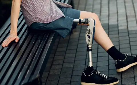 Mężczyzna z nowoczesnymi protezami nóg siedzi na ławce. Jego proteza jest zaawansowana technologicznie.