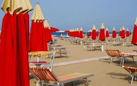 Filettate di lettini e ombrelloni rossi e gialli sulla spiaggia di Rimini Nord, pronti per accogliere i bagnanti.