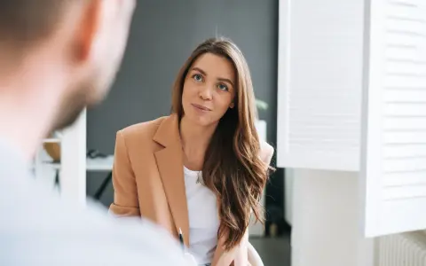 Kobieta w beżowej marynarce rozmawia z mężczyzną. Jej uśmiech sugeruje, że to miła rozmowa, być może o pracy od poniedziałku do piątku.