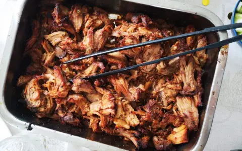 Saftigt, långkokt fläskkött i en ugnsform, perfekt för ett carnitas recept. Tång ligger redo att servera.