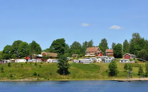 Gröna kullar med husbilar och röda stugor vid en sjö. En idyllisk plats för greans camping.