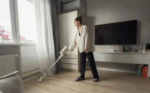 Une femme utilise un aspirateur sans fil, peut-être pour savoir quel est l'aspirateur le plus silencieux.