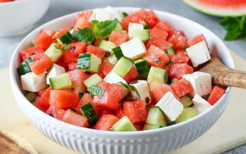 Erfrischender **Salat mit Melone**, Gurke und Feta in einer weißen Schüssel, garniert mit Minze. Perfekt für heiße Tage.