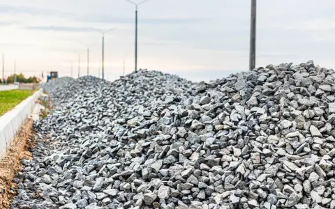 Stos kruszywa, idealnego jako składnik betonu B25, na tle słupów oświetleniowych i nieba.