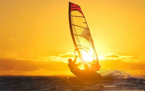 Ein Windsurfer genießt die untergehende Sonne am Ammersee. Das goldene Licht taucht die Szene in warme Farben.