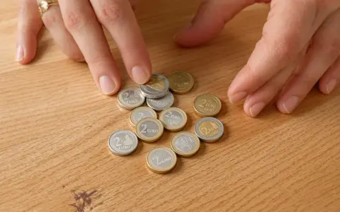 Mains disposant des pièces de 2 euros bremen 2010 sur une table en bois.