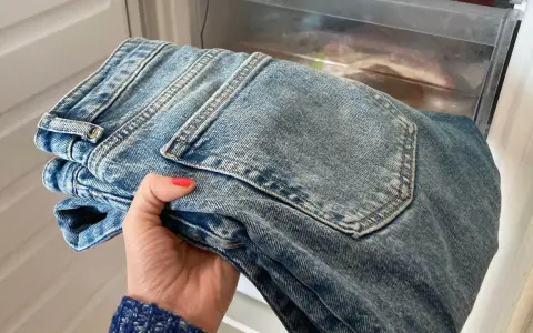 Hand håller nya jeans som luktar illa, placerade i en frys för att fräscha upp dem.