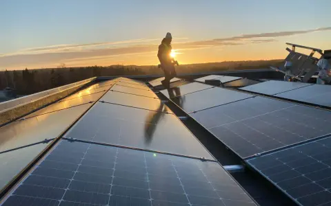 Arbetare installerar solpaneler på ett tak i solnedgången. Gosol Energi AB ser till att framtiden blir grön.