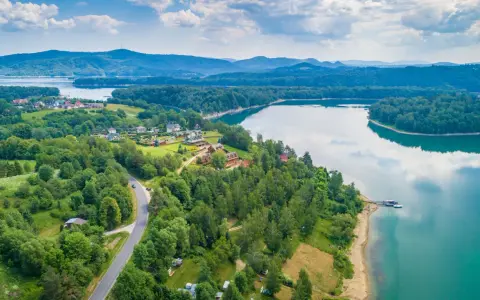 Malownicze jezioro podkarpackie otoczone lasami, z widokiem na domki letniskowe i góry w oddali.