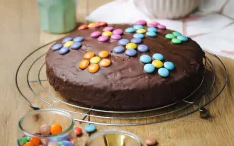 Schokokuchen mit bunten Smarties, perfekt für Kinder. Ein Glas mit weiteren Süßigkeiten steht daneben.