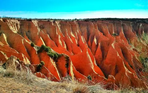 Impresionantes cárcavas en España, con formaciones rojizas y vegetación escasa bajo un cielo azul intenso.
