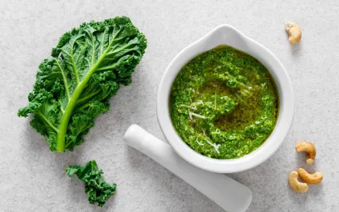 Pesto z jarmużu do słoika, gotowe do przechowywania. Obok liść jarmużu i orzechy nerkowca.