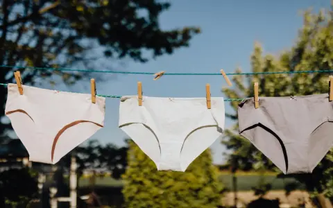 Drei Unterhosen in verschiedenen Grautönen trocknen an einer Wäscheleine. Das Bild zeigt den Prozess des Unterhosen waschen.