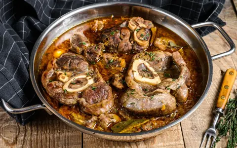 Ossobuco que es: jugosas rodajas de ternera cocinadas a fuego lento en una rica salsa con hierbas y especias, servidas en una sartén metálica.