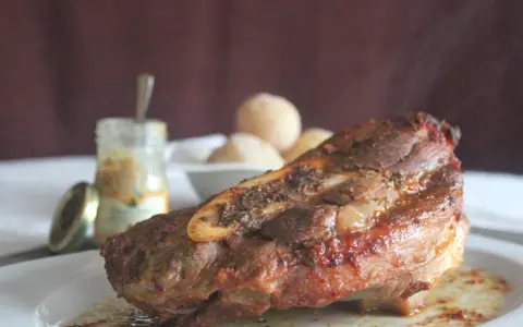 Costilla de ternera asada jugosa con hueso, servida en plato blanco con salsa y guarnición.