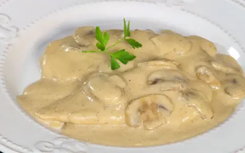 Pollo cremoso con champiñones y perejil en un plato blanco.