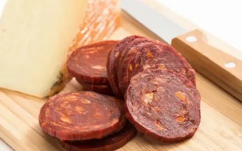 Plasterki pikantnego chorizo, kawałek sera i nóż na desce. Idealne na przekąskę, zastanawiasz się chorizo co to?