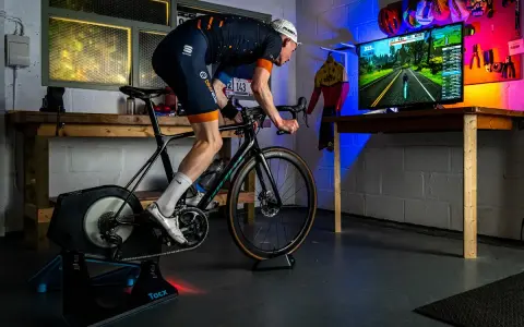 Cyclist on a Tacx trainer, connected to a TV displaying a Zwift course. This setup showcases Zwift compatible devices for an immersive indoor cycling experience.