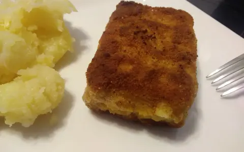 Chrupiąca panierowana kostka rybna z purée ziemniaczanym na białym talerzu.