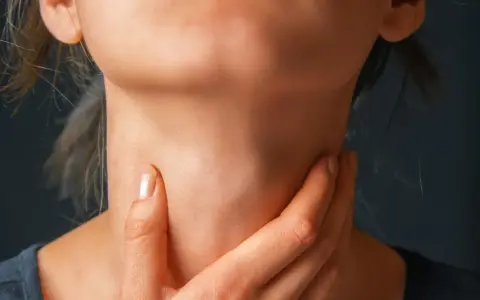 Zbliżenie na szyję osoby trzymającej się za gardło.