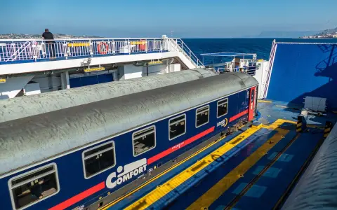 Ein blauer Nachtzug nach Palermo steht auf einer Fähre. Ein Mann blickt aufs Meer.