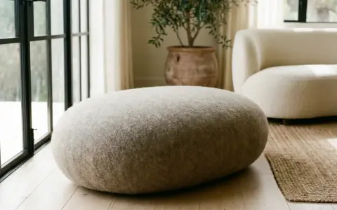 Un morbido pouf dal design organico, rivestito in tessuto grezzo, si abbina a un divano bouclé e a un vaso in terracotta.