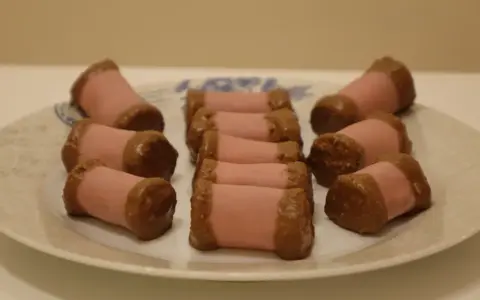 En tallrik med rosa marsipanbakelser doppade i choklad. Dessa små godsaker, som ser ut som en dammsugare i långpanna, är redo att avnjutas.