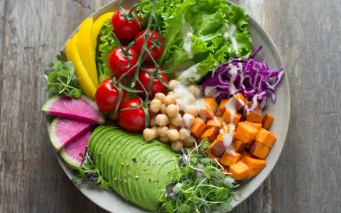 Une assiette colorée avec avocat, tomates, pois chiches, patates douces, chou rouge, radis et poivron jaune. Une belle idée de salade composée.