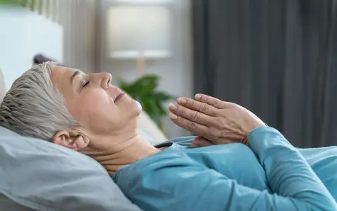 Frau liegt entspannt im Bett, Hände vor der Brust gefaltet. Sie praktiziert eine Technik, die wirkt Meditation im Schlaf.