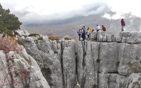 Grupa turystów na skalnym szczycie, podziwiająca widok na góry. Może to być okolica stolicy Czarnogóry, Podgoricy.