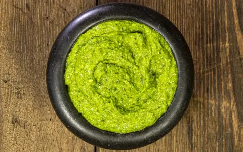 Pesto genovese ricetta originale in un mortaio di pietra, su un tavolo di legno rustico. Fresco e profumato.