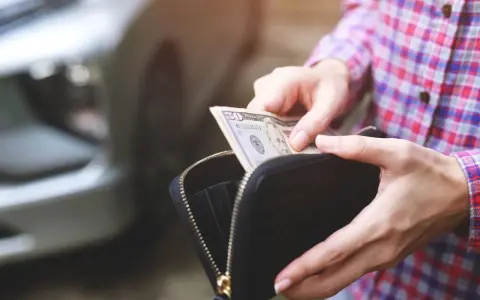 Ręce wyciągają banknot 50 dolarów z portfela. W tle widać fragment samochodu, sugerując kupno samochodu za gotówkę.