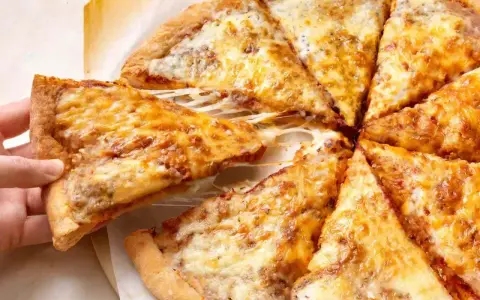 Pyszne, gorące ciasto na pizzę z ciągnącym się serem, które właśnie jest podnoszone.