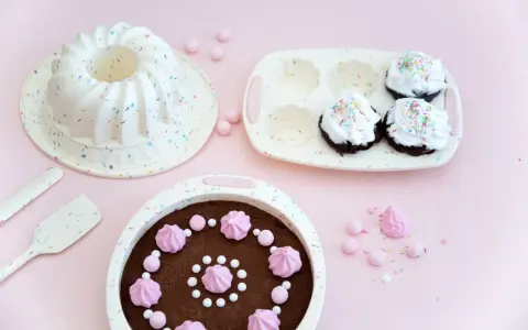 Förberedelser för ett härligt baka kalas! En sockerkaksform, muffinsform och en färdig chokladkaka med rosa maränger och strössel.