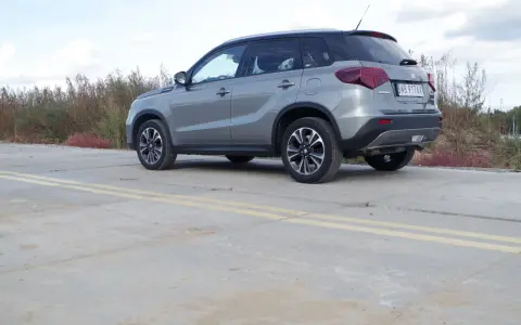 Szary Suzuki Vitara Hybrid z czarnym dachem stoi na betonowej nawierzchni z żółtymi pasami.