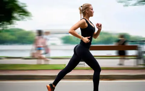 Donna bionda in abbigliamento sportivo nero corre con una postura corsa perfetta lungo un percorso alberato.