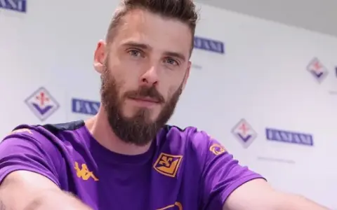 David de Gea, con barba y camiseta morada, posa ante un fondo con logos.