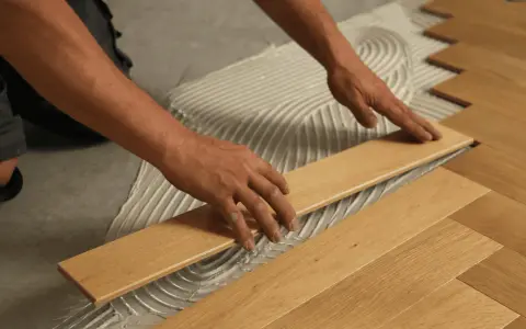 Man's hands carefully placing a wooden plank during the installation of floating flooring.