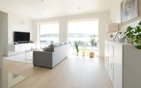 Ett ljust vardagsrum med en grå soffa, ett runt soffbord och en vit förvaringsmöbel. En lampa med vitt ljus lyser upp rummet.