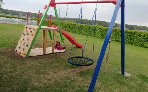 Plac zabaw z wspinaczką, zjeżdżalnią, huśtawkami i okrągłą huśtawką.