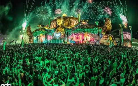 Folla immensa sotto un palco spettacolare con fuochi d'artificio verdi, uno dei rave party più famosi al mondo.